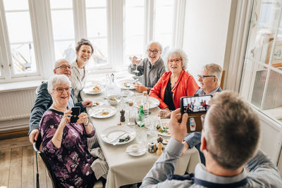 Waiter clicking photograph of senior friends sitting in restaurant