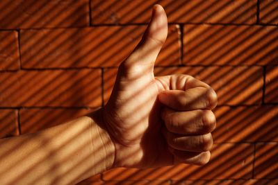 Close-up of hand showing thumbs up against brick wall