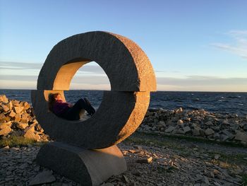 Man on retaining wall by sea against clear sky