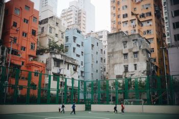 Boys playing soccer at court against buildings