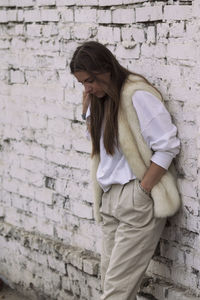 Full length of young woman standing against brick wall