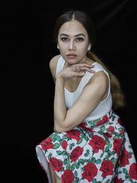 Portrait of young woman standing against black background