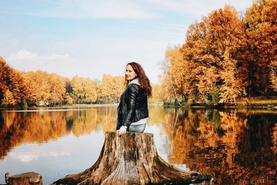 Portrait of woman sitting at lakeshore against trees