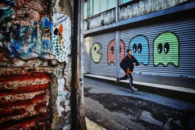 Rear view of man walking against graffiti wall
