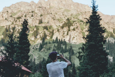 Rear view of man photographing while standing against mountain