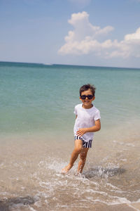 Boy child in striped shorts and a white t-shirt walks on a sandy beach and in sunglasses