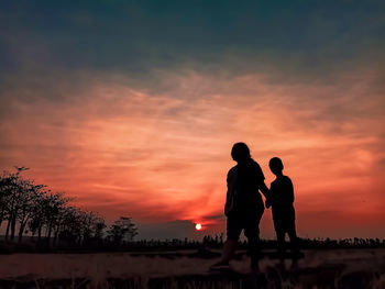 Silhouette mother and son walking on land against orange sky during sunset
