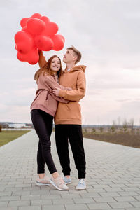 Valentines day. young loving couple hugging and holding red heart shaped balloons outdoors