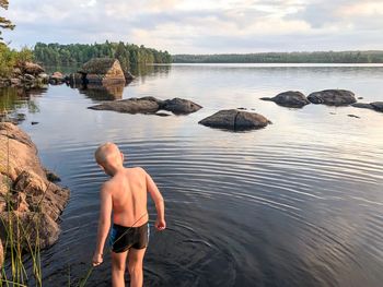 Rear view of shirtless man standing on rock by sea against sky