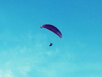 Low angle view of person paragliding against blue sky