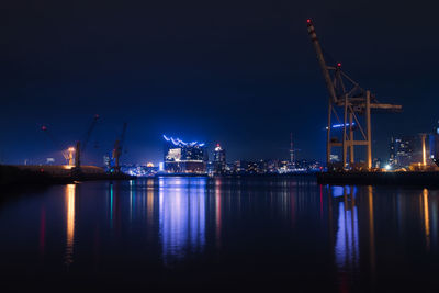 Illuminated pier by harbor against sky at night