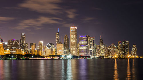 Illuminated cityscape by river against sky at night