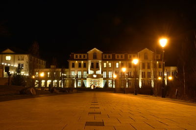 Illuminated street amidst buildings against sky at night