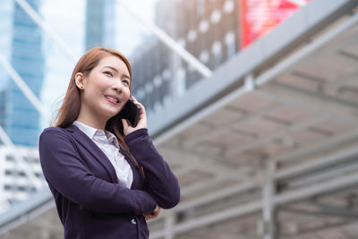 Smiling young businesswoman talking on mobile phone while standing outdoors