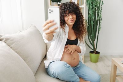 Young woman using mobile phone while sitting on bed at home