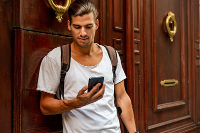 Young man using mobile phone by wooden door