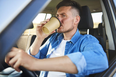 Man drinking coffee while sitting in car