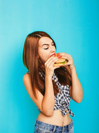 Young woman eating against blue sky