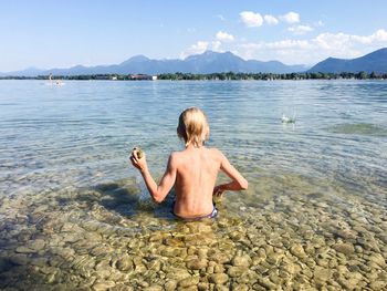 Rear view of shirtless boy in lake against sky