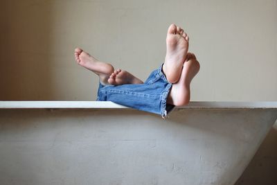 Low section of people in bathtub against wall