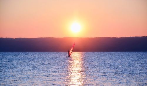 Silhouette person on sea against sky during sunset