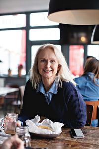 Portrait of smiling mature woman sitting at dining table in restaurant
