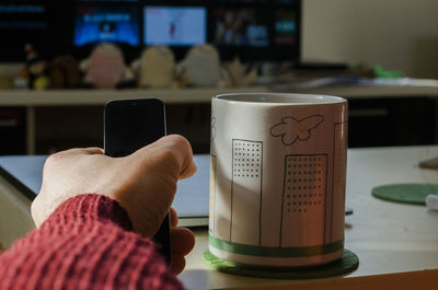 Cropped hand of woman holding mobile phone at home