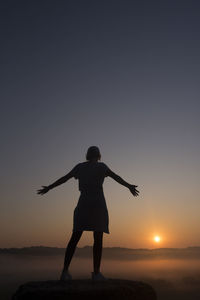 Silhouette of girl at mountain top with outstretched arms at sunrise