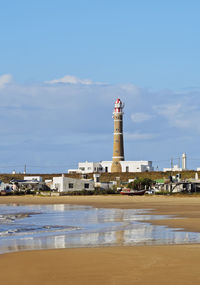 Lighthouse by sea against buildings against sky
