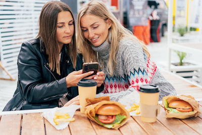 Portrait of smiling friends using mobile phone while sitting on table