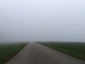 Empty road amidst field against sky during foggy weather