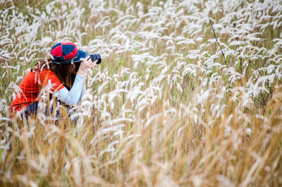 Side view of woman photographing amidst plants on field