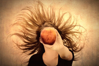 Woman with tousled hair holding apple over face