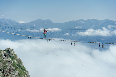A person walks on a suspended rope bridge in the clouds. extreme attraction.
