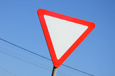 Low angle view of road sign against clear blue sky