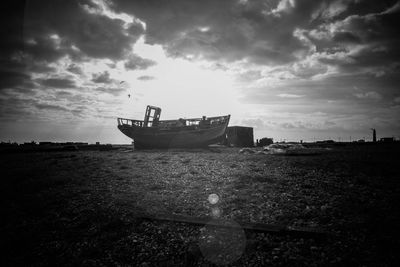 Abandoned boat on field against cloudy sky