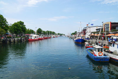 Boats moored in canal at harbor against sky