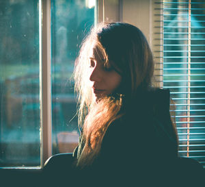 Side view of young woman standing by window