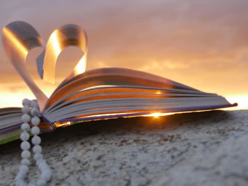 Low angle view of heart shape book pages with necklace against sky during sunset