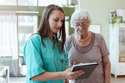 Female healthcare worker showing digital table to senior woman in nursing home