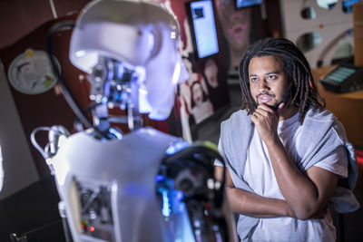 Thoughtful technician with hand on chin looking at human robot in workshop