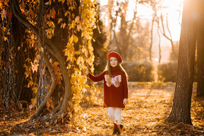 Cute six year old girl in burgundy clothes and a beret walks through the autumn park at sunset