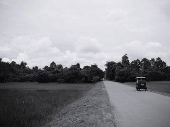 Road amidst trees on field against sky