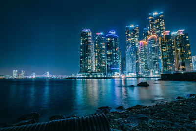 Illuminated city by sea against sky at night