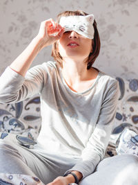 Young woman in grey pajama and sleeping mask in shape of cute sleeping cat face. 