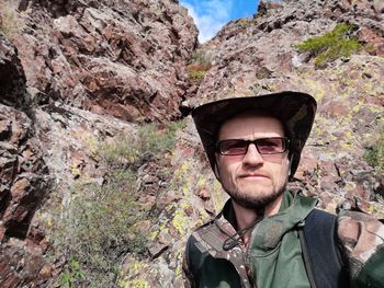 Portrait of man wearing sunglasses standing against rock mountain