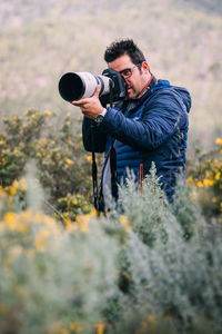 Full length of man holding camera while standing on field