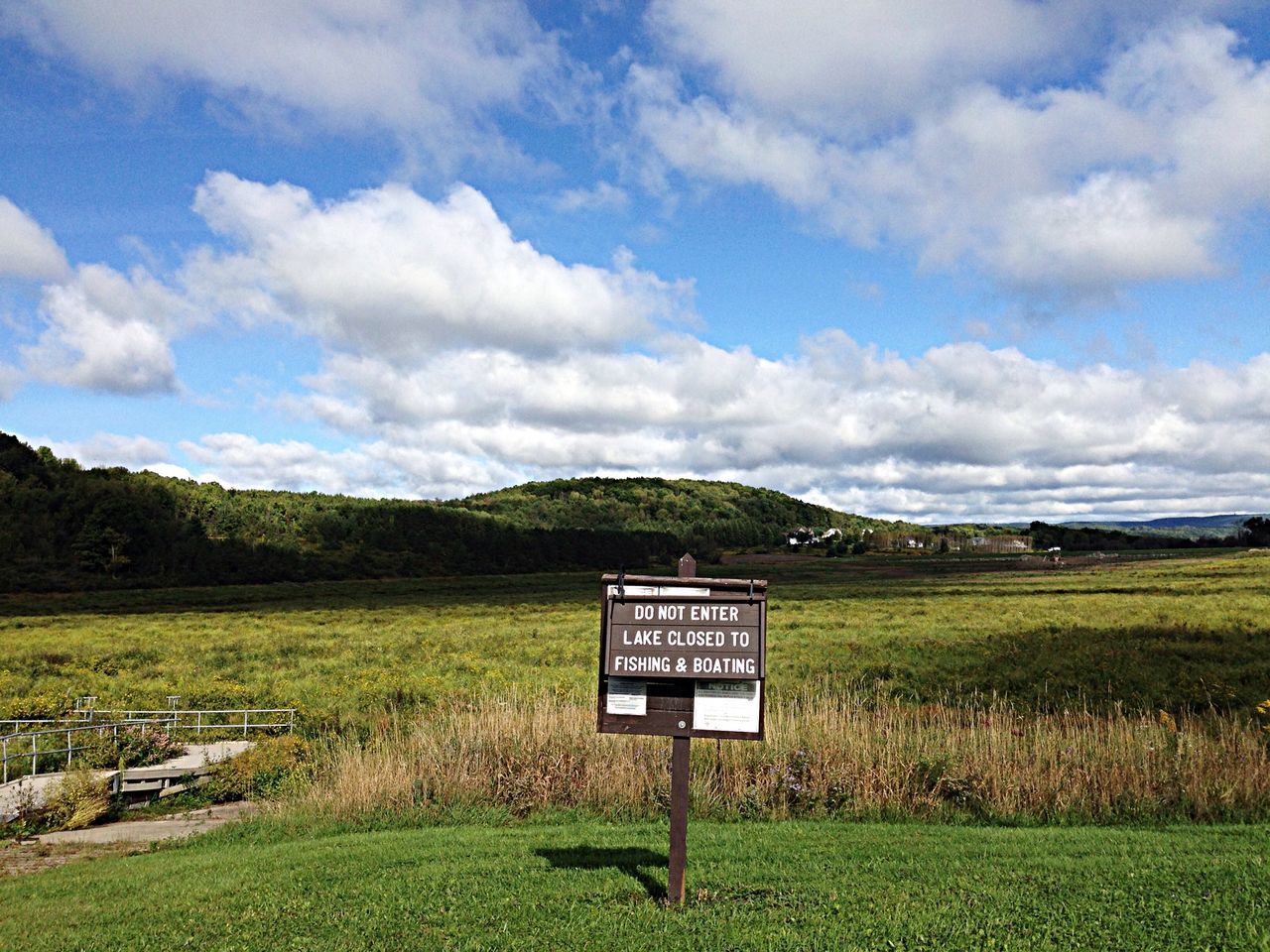 grass, landscape, field, text, sky, communication, western script, tranquil scene, tranquility, scenics, grassy, information sign, nature, cloud - sky, beauty in nature, rural scene, green color, cloud, sign, day