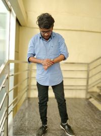 Full length of young man looking time in wrist watch while standing on staircase