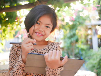 A happy asian girl enjoys using a tablet outdoors with a stylus pen in her hand